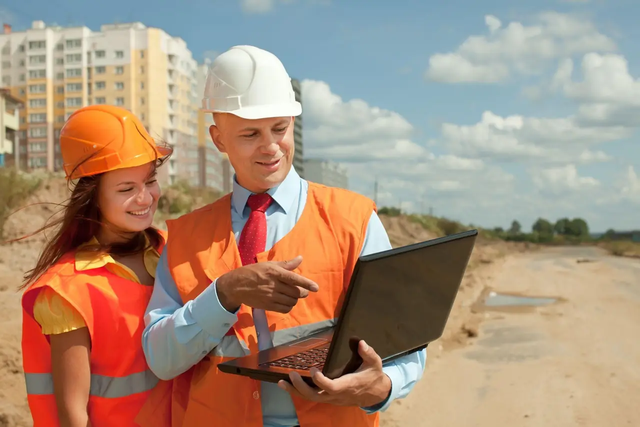 Two contractors in hi-vis vests reviewing construction lead data on a laptop at a job site
